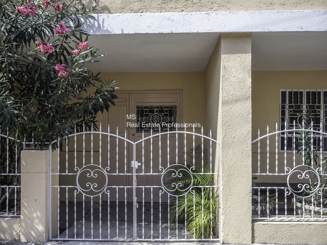 A white metal gate with smiley faces in front of a beige building.