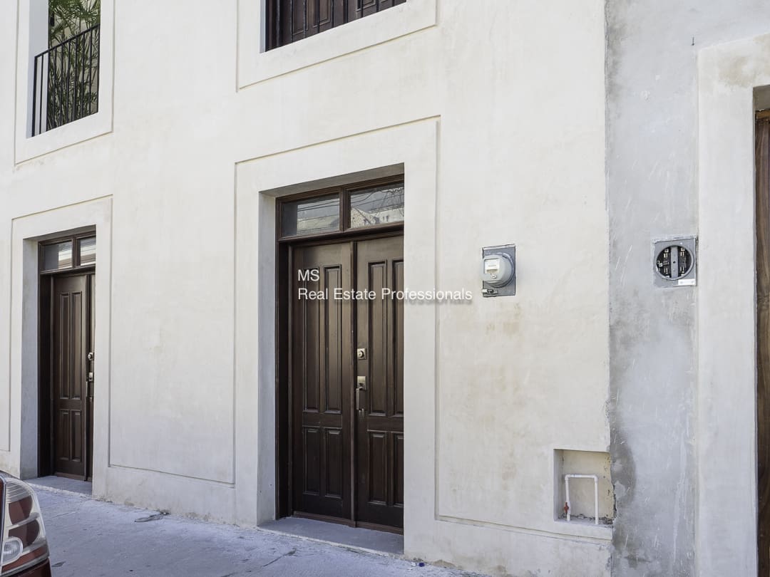 A dark brown door set in a light-colored wall on a street.