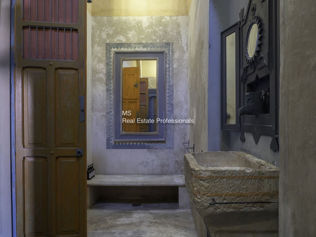 A dimly lit room with a bench, mirror, and ornate stone structures.