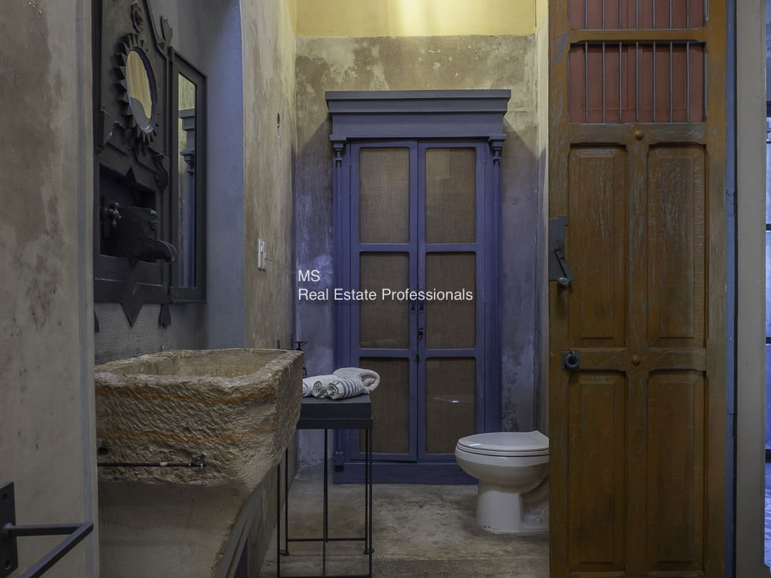 A rustic bathroom with stone walls, a blue door, and a simple toilet.