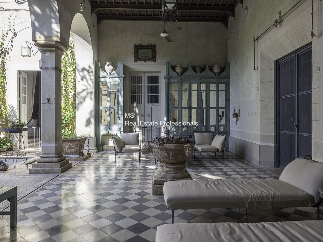 A sunlit vintage veranda with cushioned seating and a stone fountain.