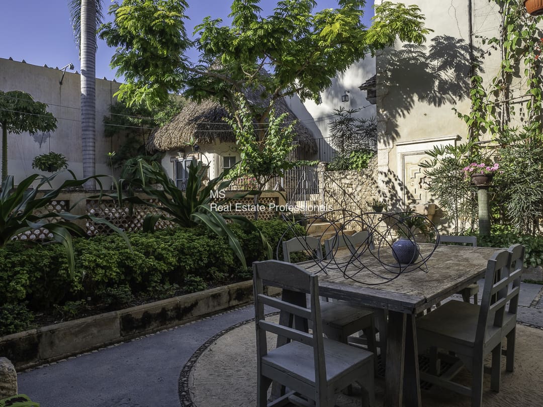 A stone garden table with chairs under a tree in a sunny courtyard.