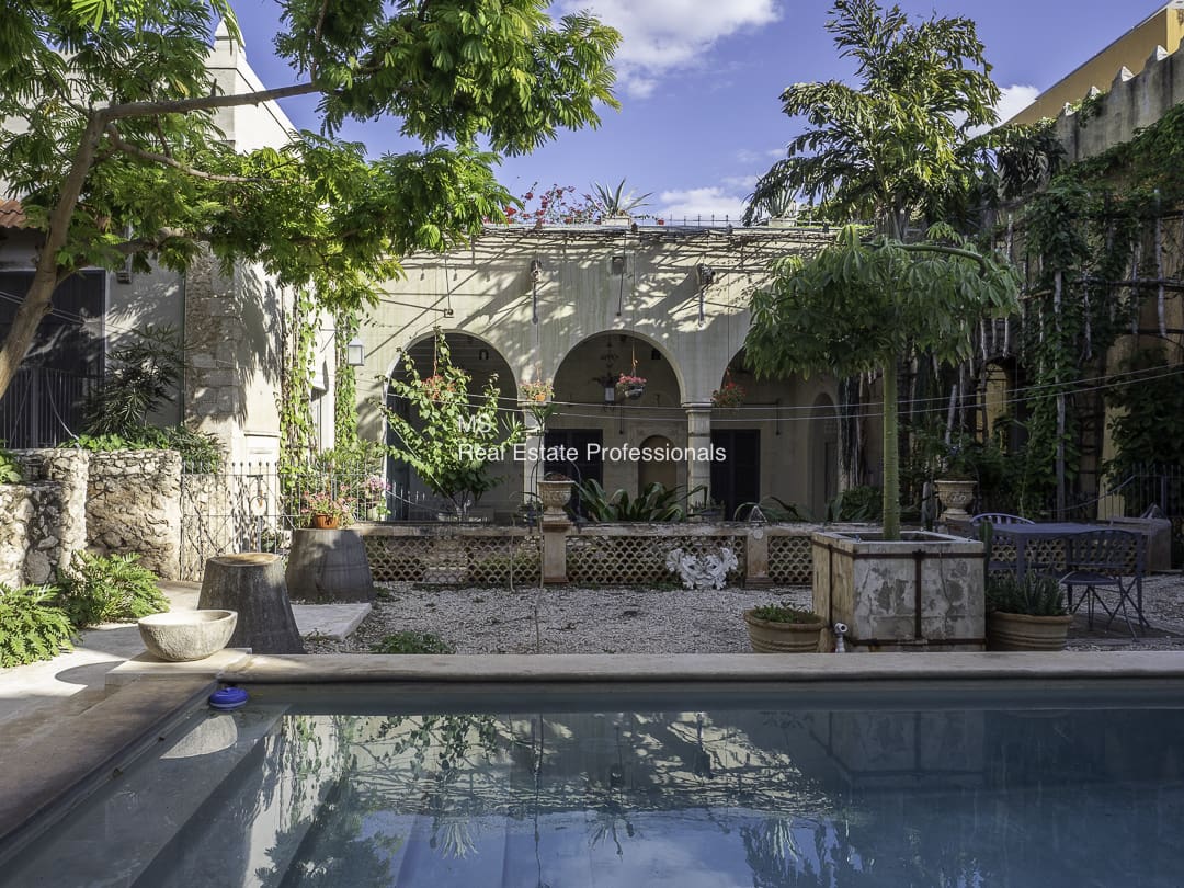A serene courtyard with arches, greenery, and a pool reflecting the sky.
