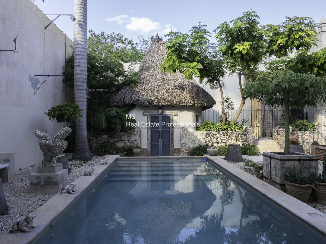 A serene backyard pool with a thatched roof hut and lush greenery.