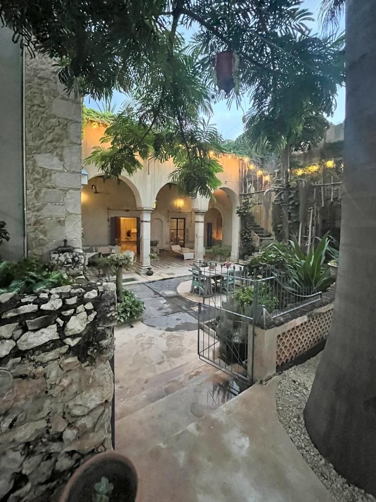 A serene courtyard with stone walls and lush greenery under a bright sky.