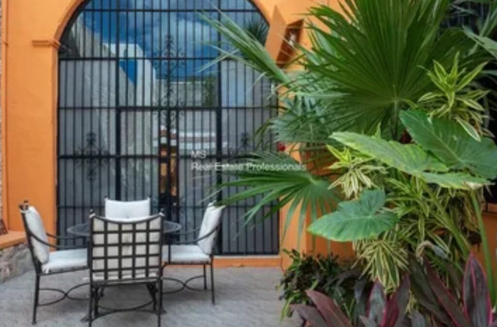 A patio with chairs and plants in front of an iron gate.