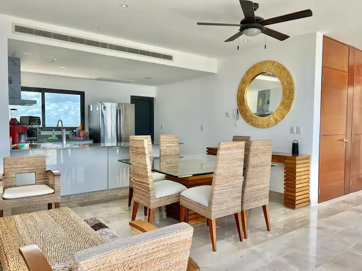 A modern dining area with wicker chairs and a round mirror.