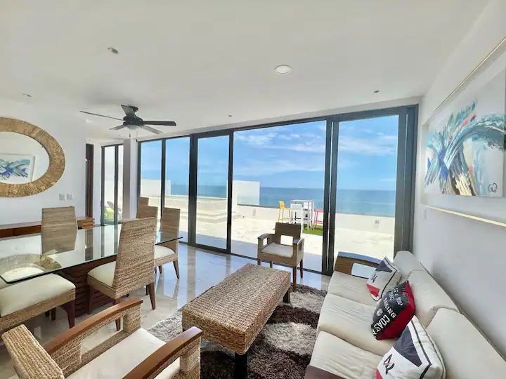 Bright living room with large glass doors opening to a sunny balcony overlooking the ocean.