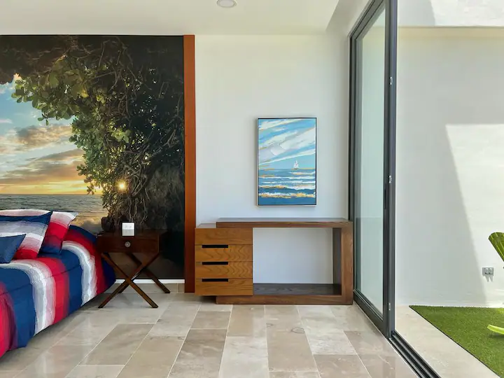 A modern desk with a large painting and a chair in a sunlit room.