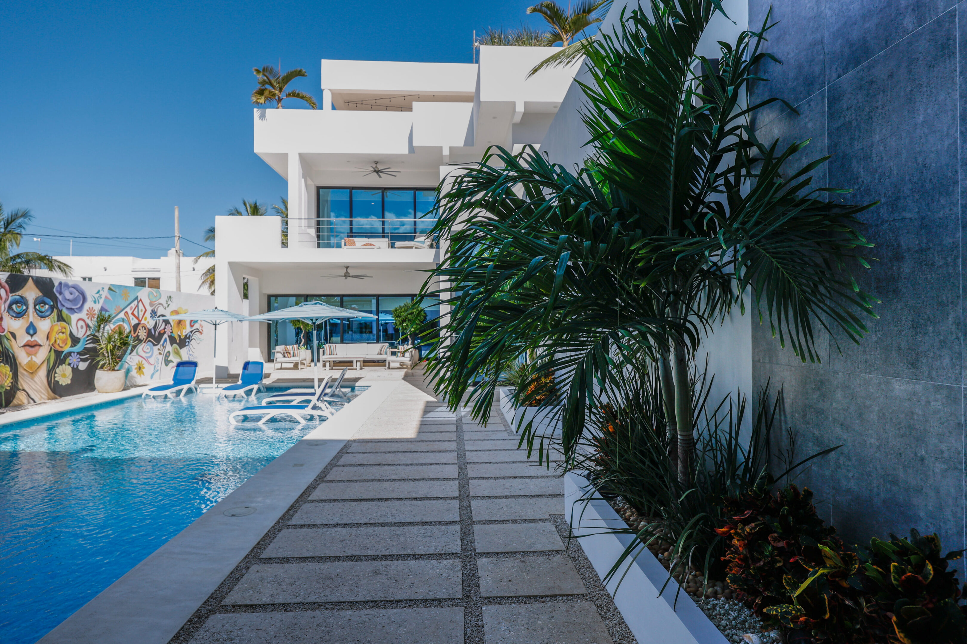 Modern house with swimming pool and palm trees under clear blue sky.