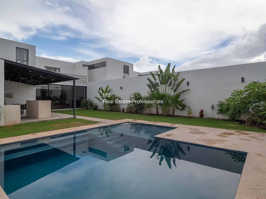 A pool with a large white wall and a patio.