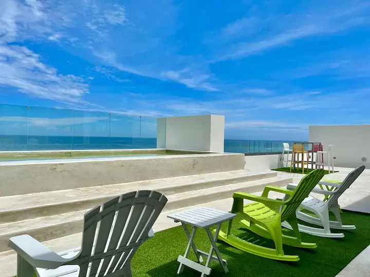 A modern terrace with lounge chairs overlooking the ocean under a bright blue sky.