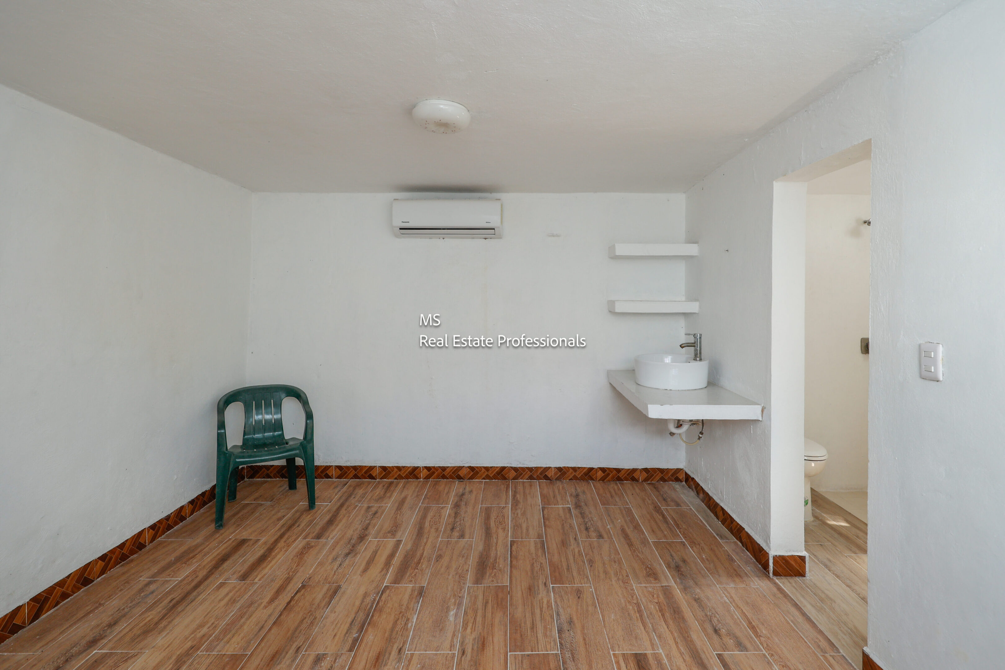 Empty room with wood floor, sink, and chair.