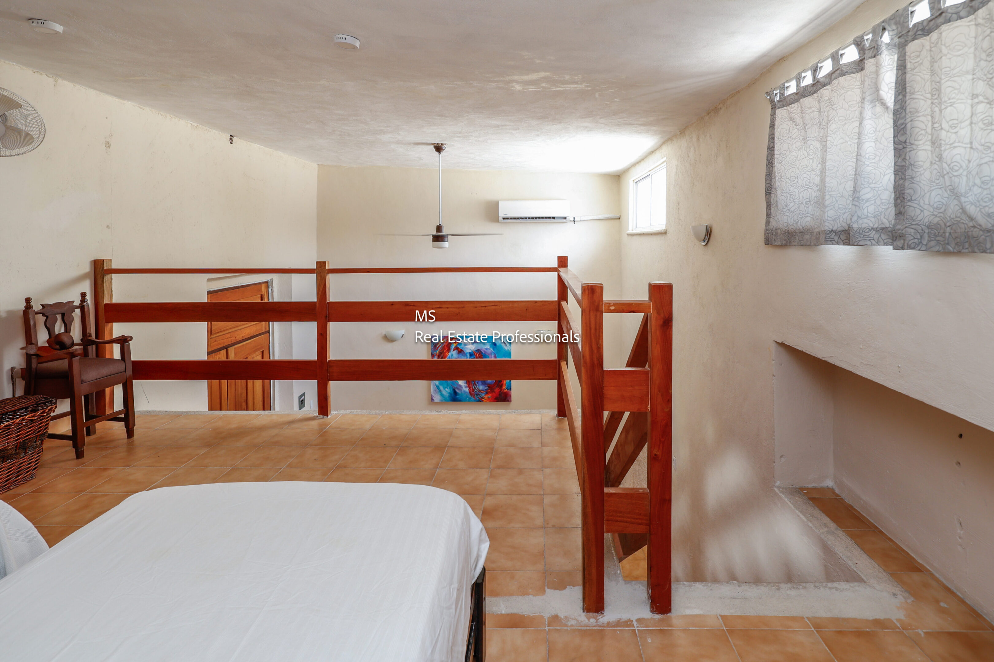 Loft bedroom with wooden stairs and fan.