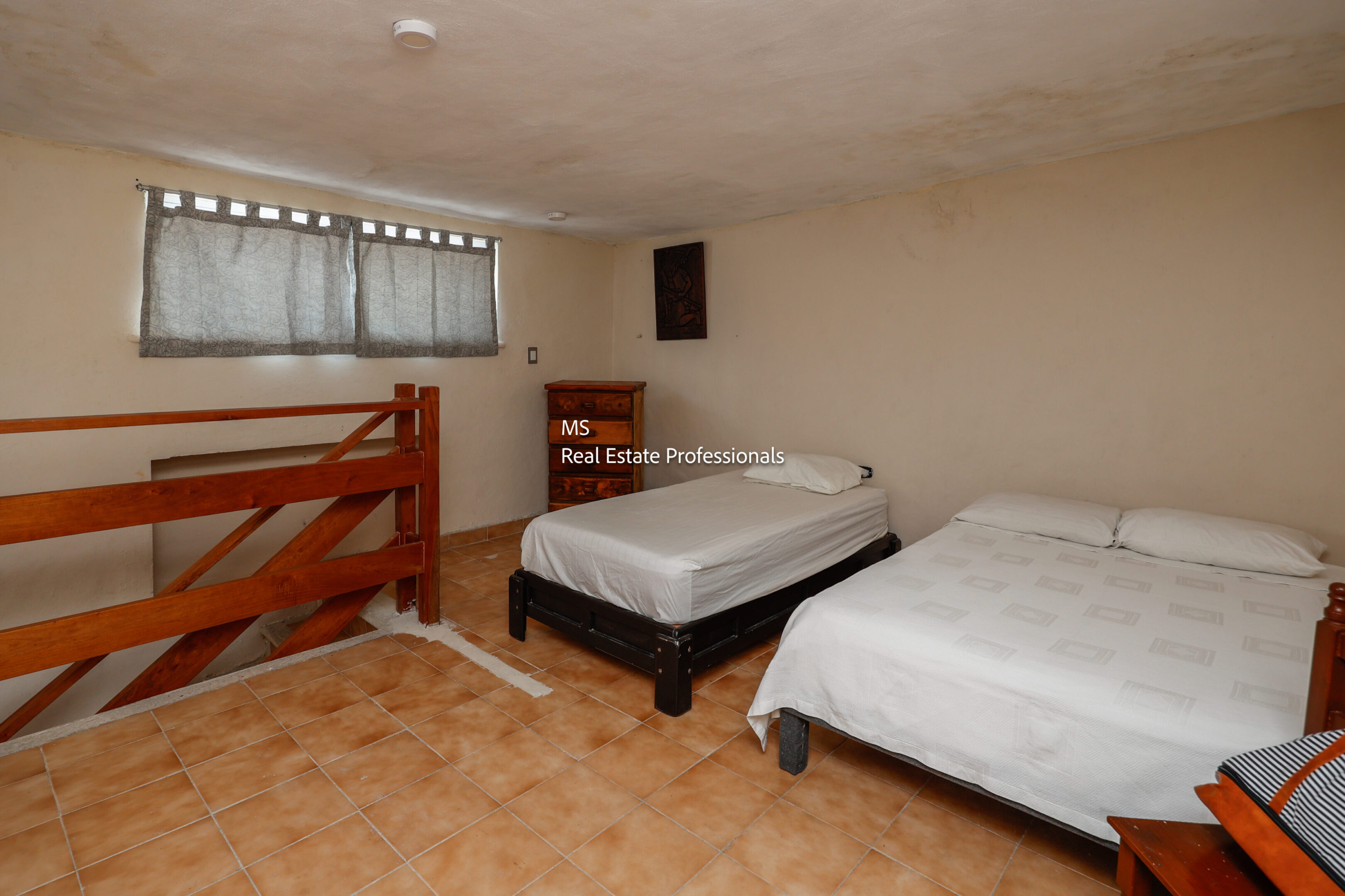 Small bedroom with two beds and wooden railing.