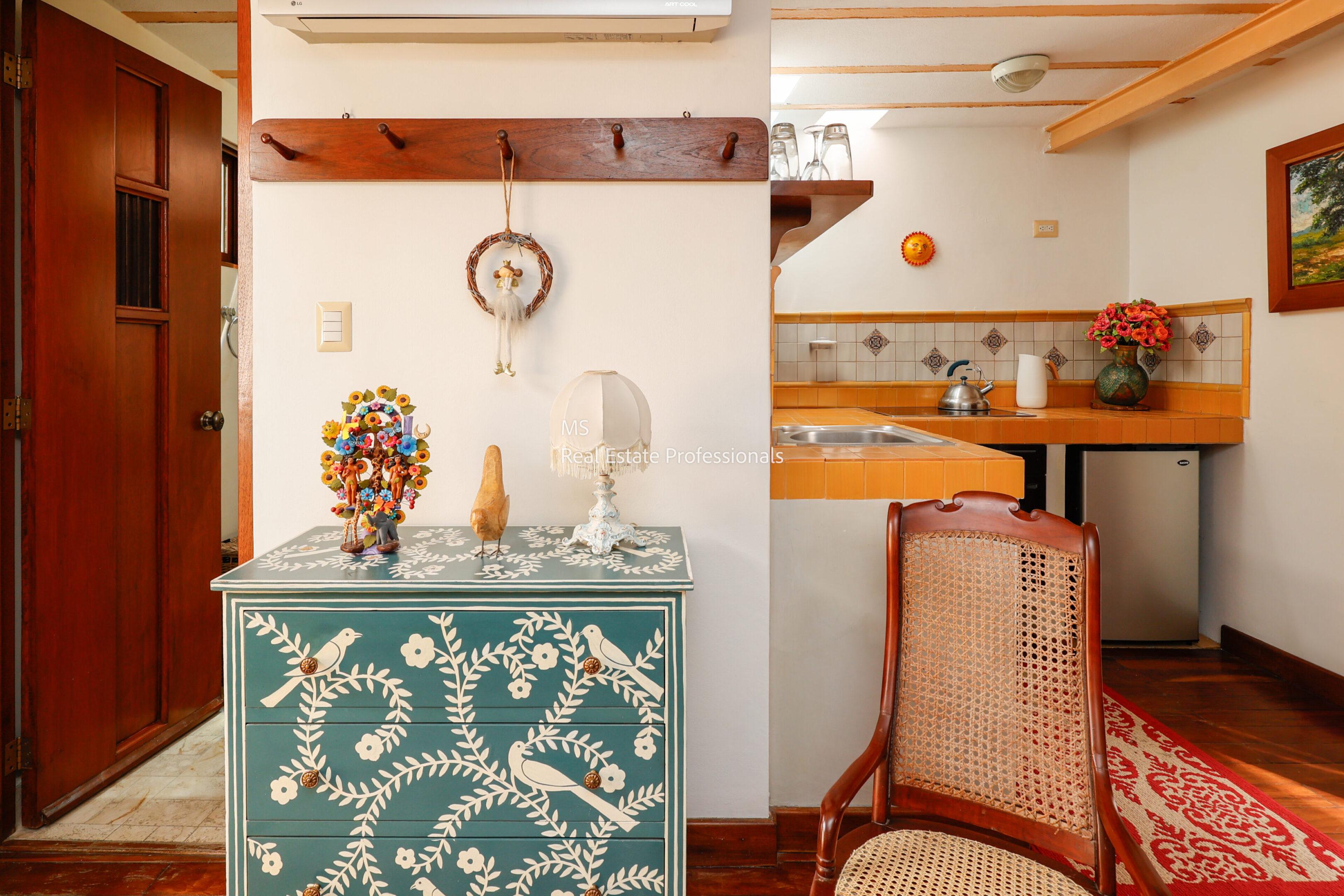 Ornate dresser, chair, kitchenette in room.