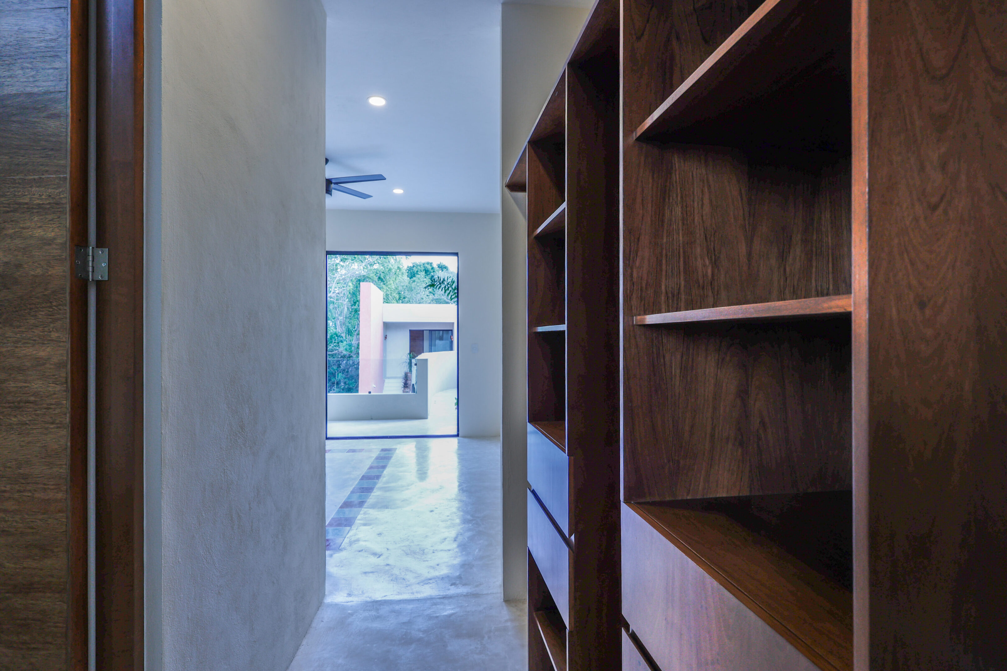 Narrow hallway with wooden shelves and an open door leading outside.