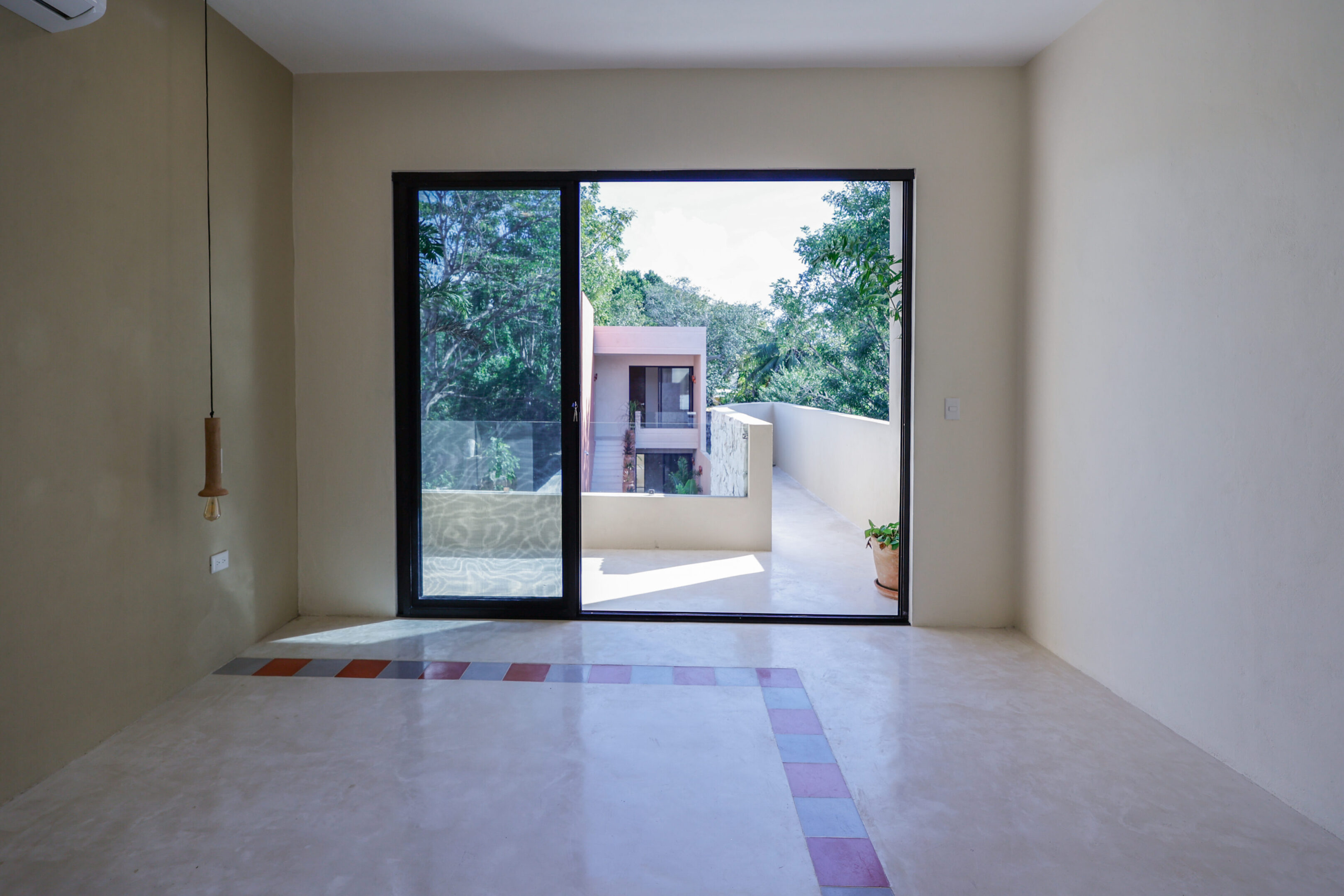 Empty room with large glass doors opening to a balcony and greenery.