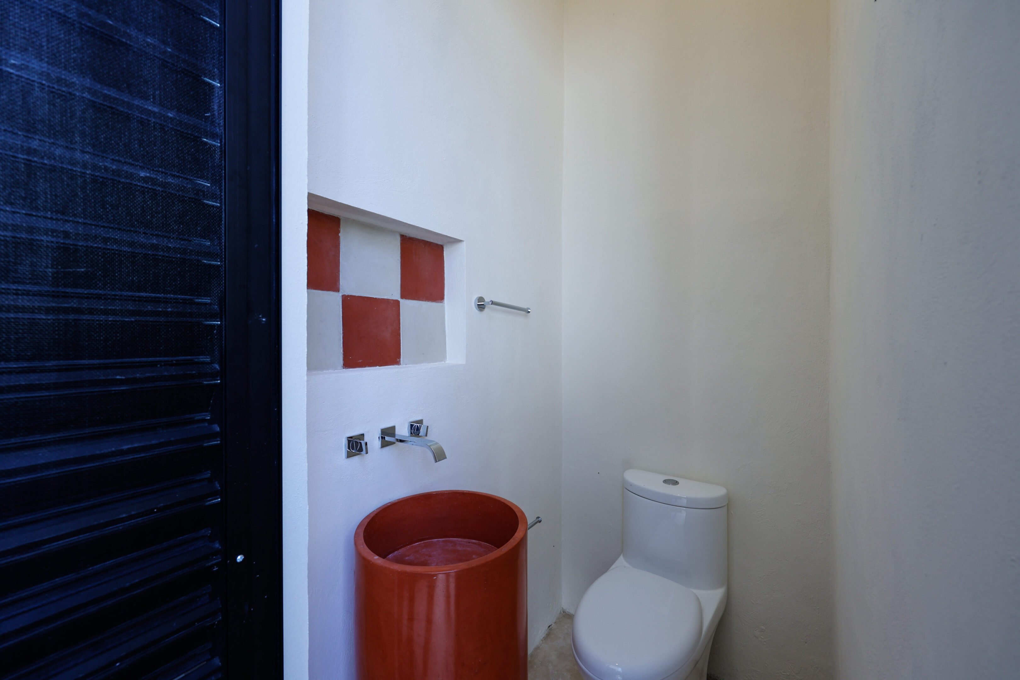 Small bathroom with red bucket and white toilet.