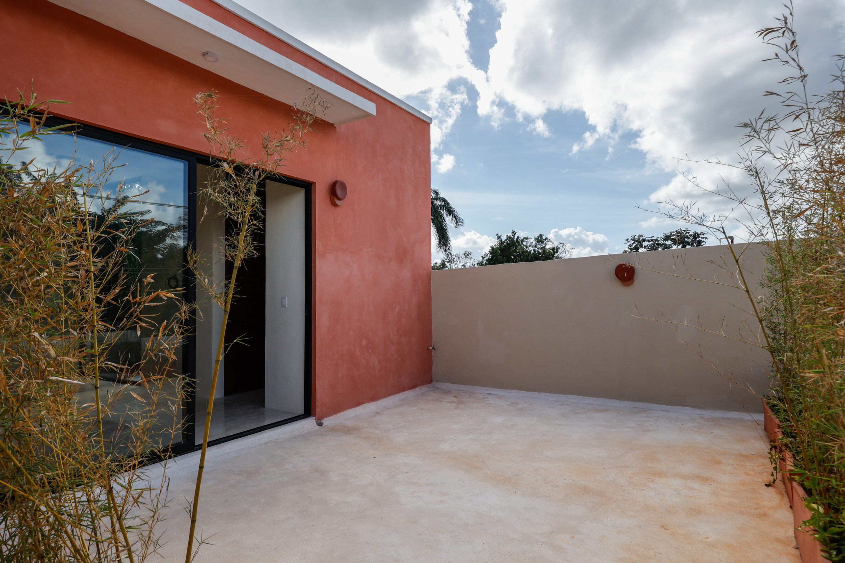 A sunny rooftop terrace with red walls and a sliding glass door.