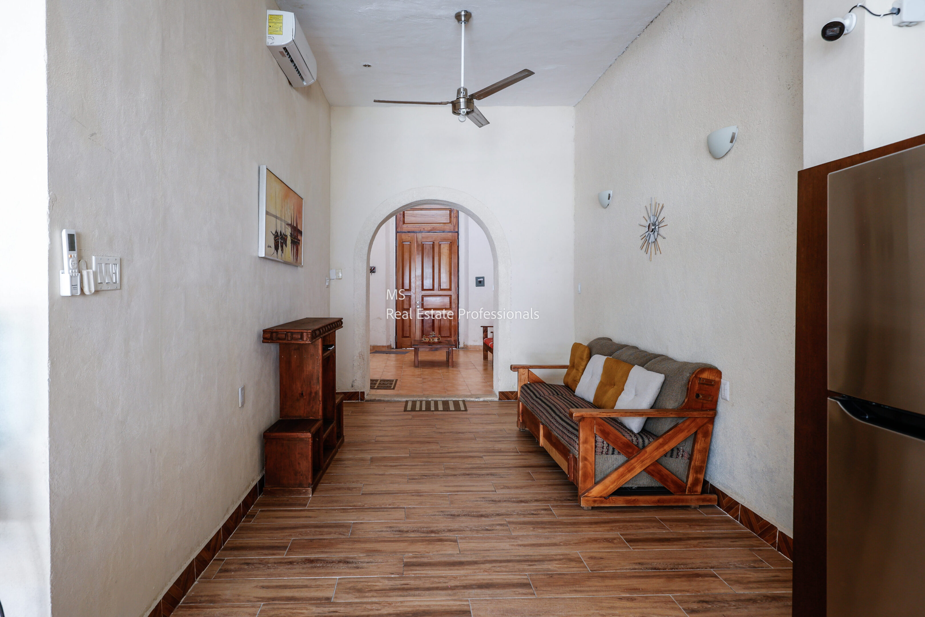 A narrow living room with wooden floor and simple furniture.