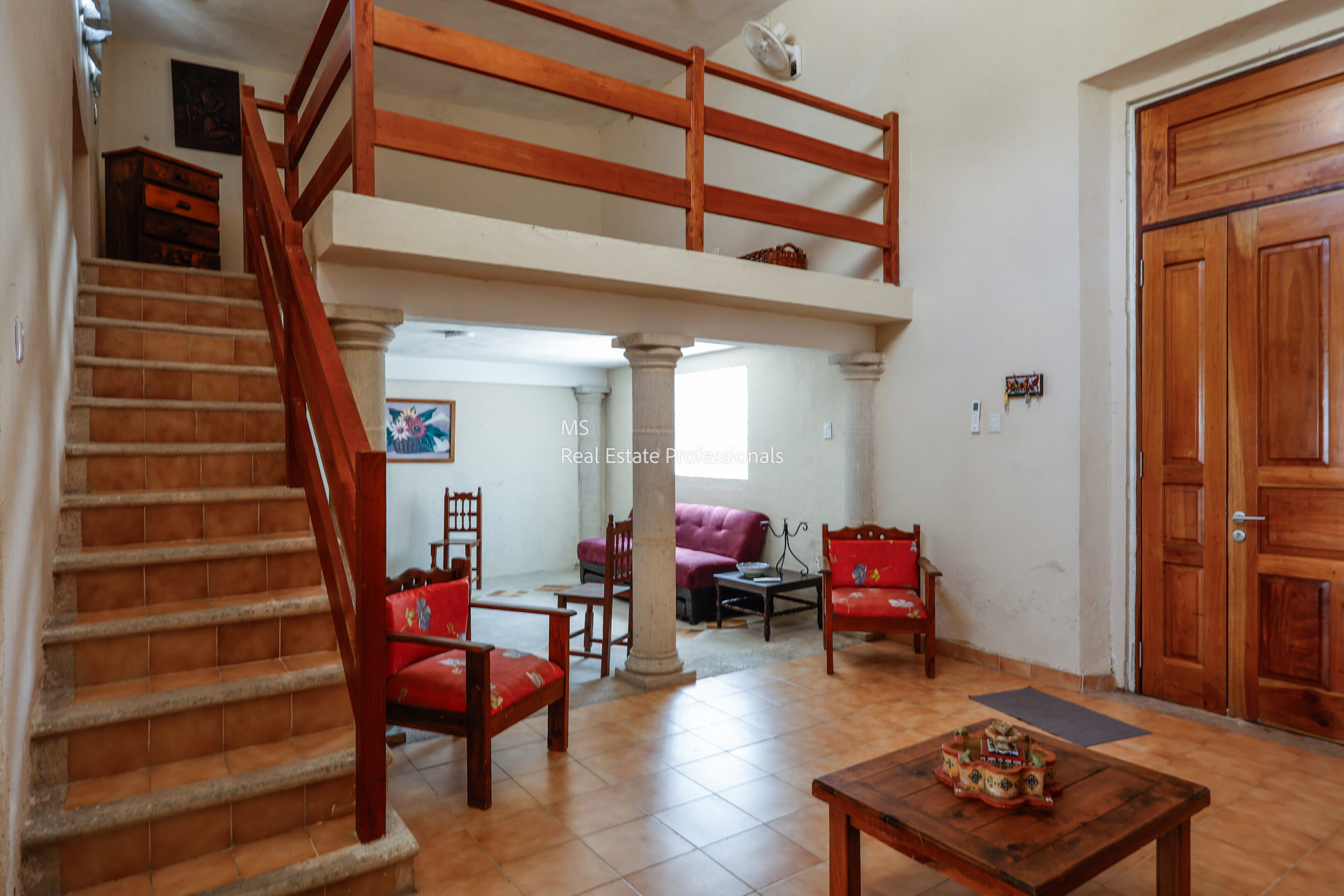 Cozy living room with wooden stairs and red chairs.