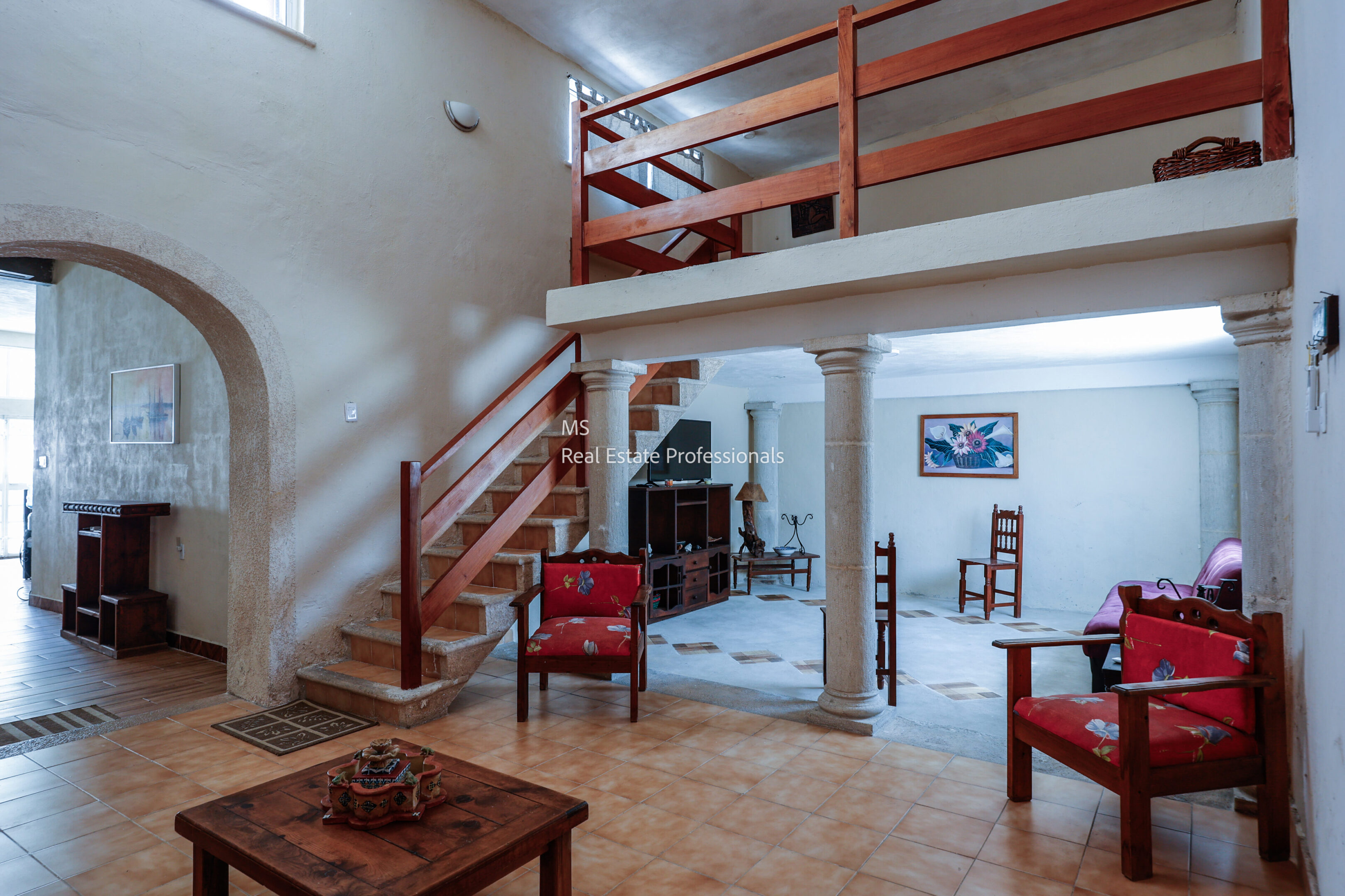 Cozy living room with wooden staircase and red chairs.