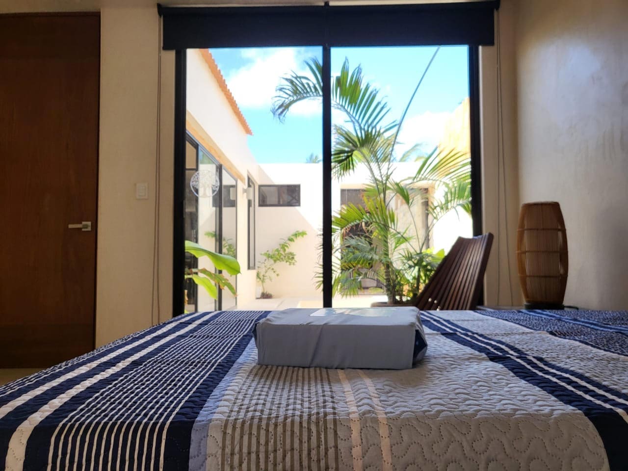 A neatly made bed with a towel in front of a large glass door.