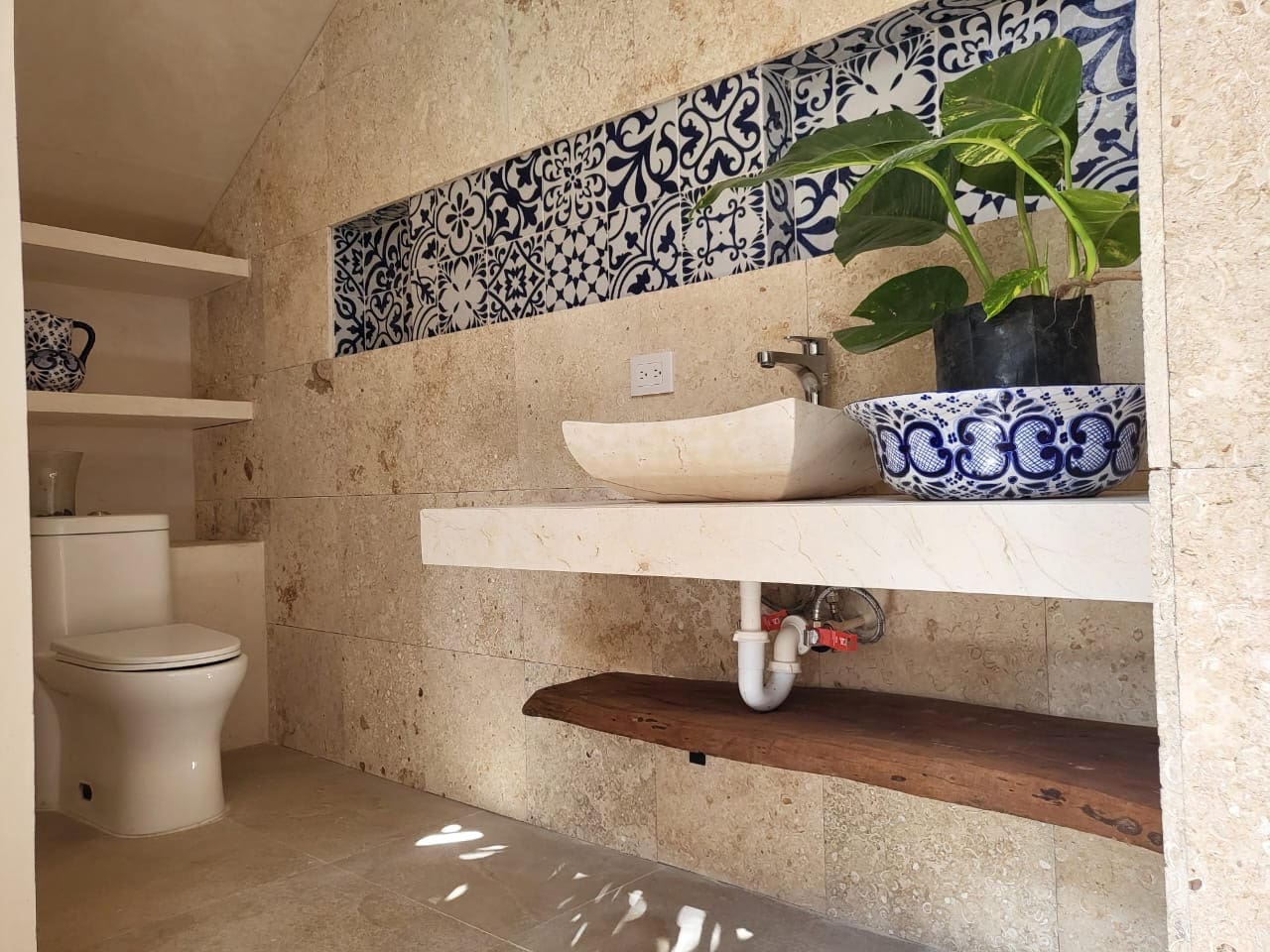 A stylish bathroom with a beige stone wall, blue patterned tiles, and a blue ceramic sink.