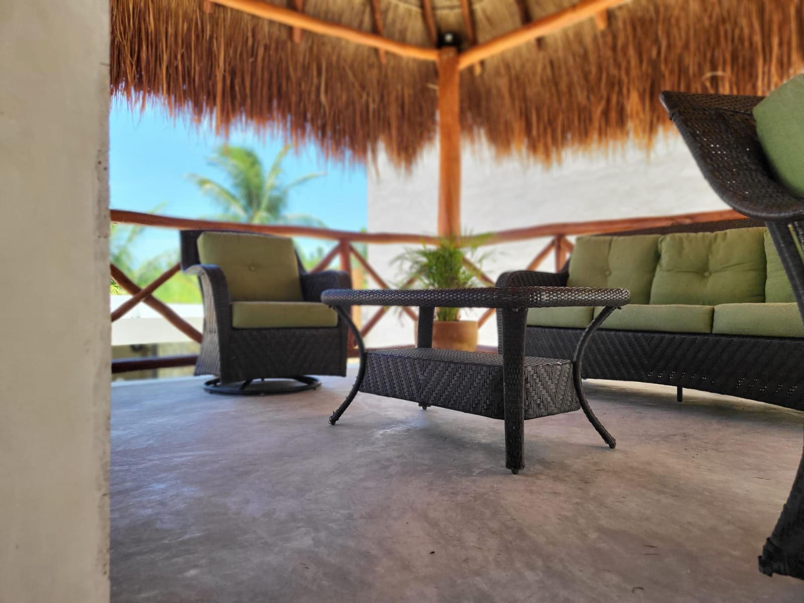 Outdoor seating area with cushioned chairs under a thatched roof.