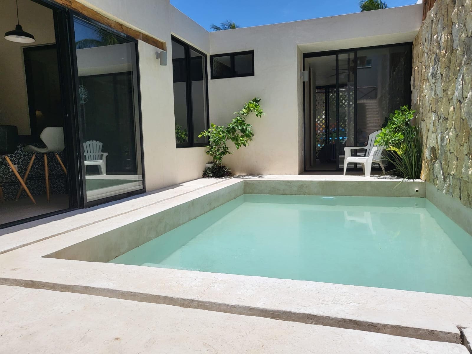 A modern backyard pool with clear water and white patio furniture.