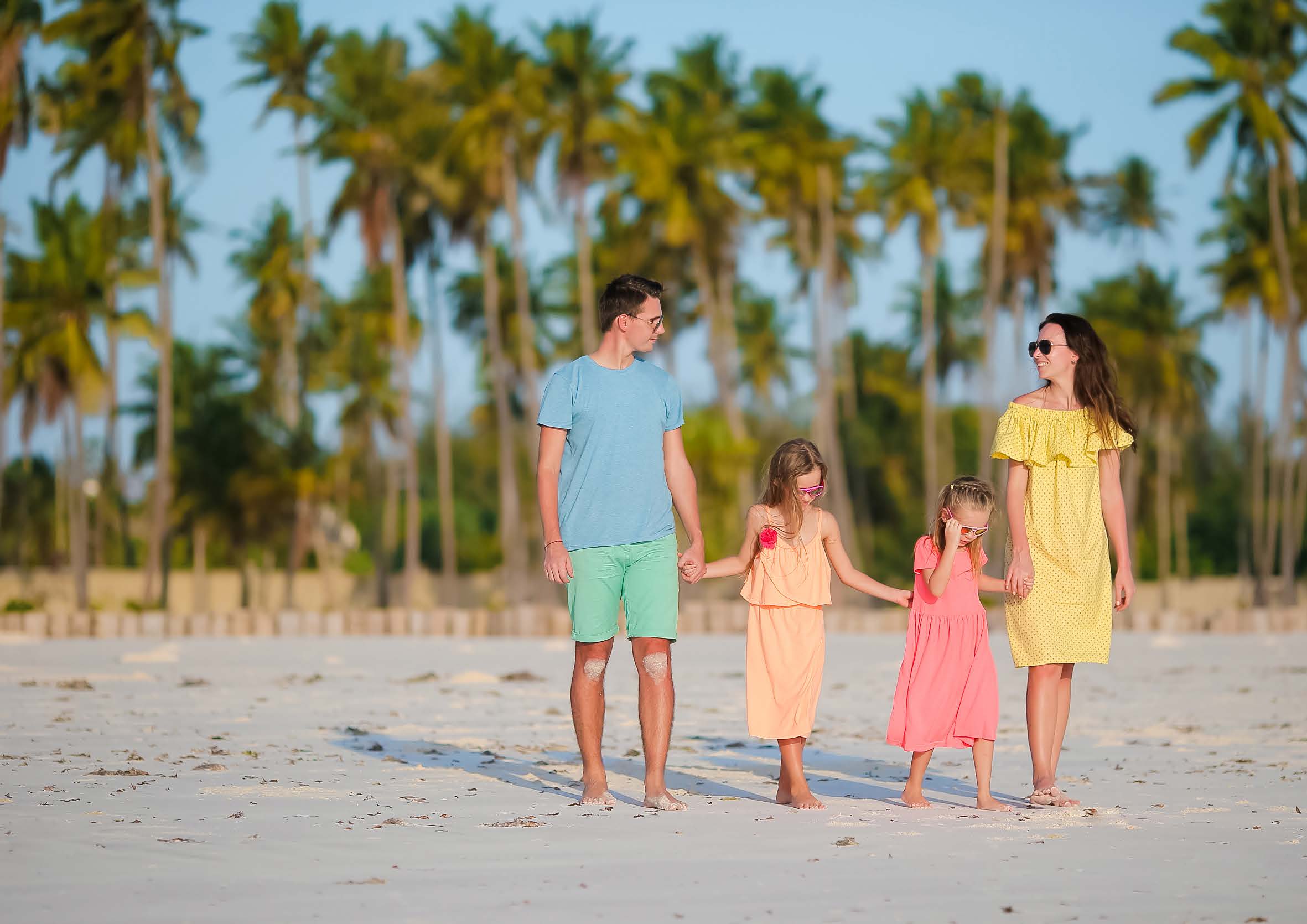 A family of four walking on a beach with palm trees.
