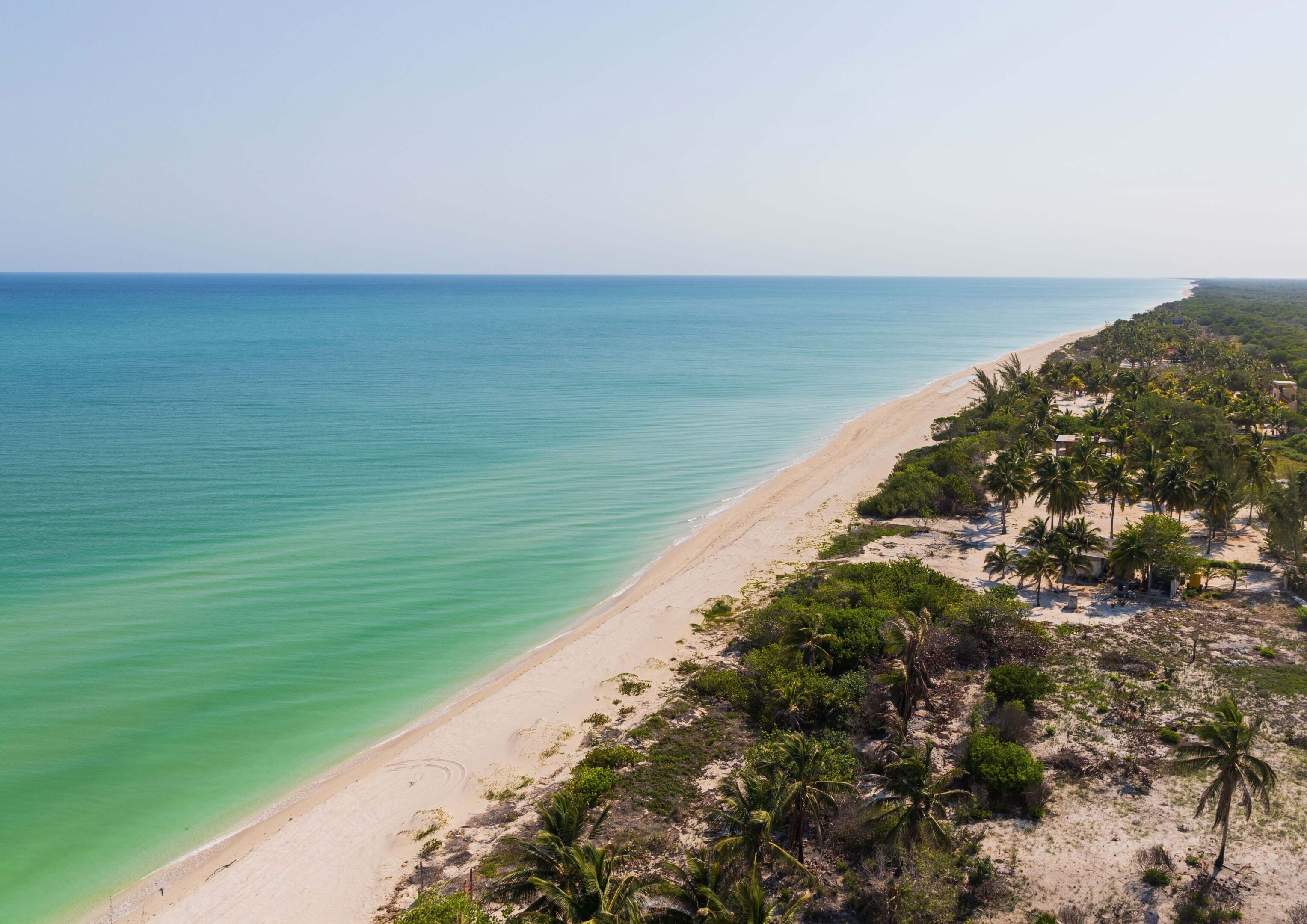 Aerial view of a sandy beach with clear turquoise water and greenery.