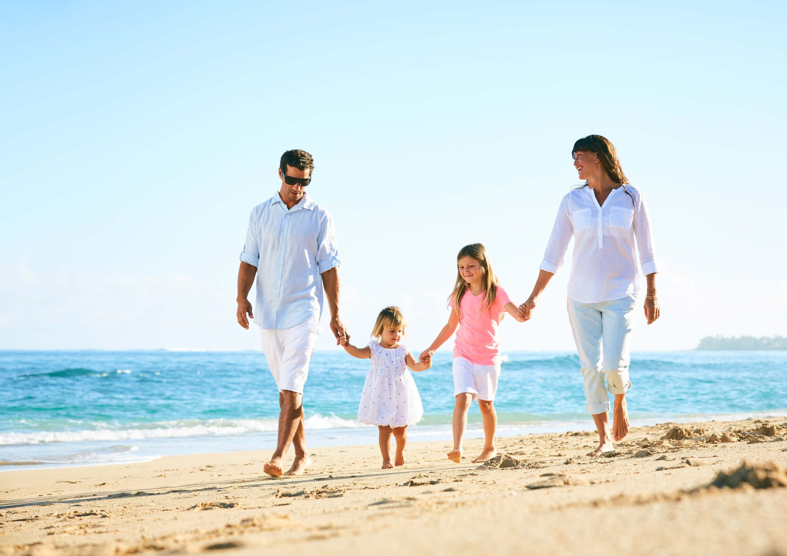 Family of four walking on the beach holding hands.