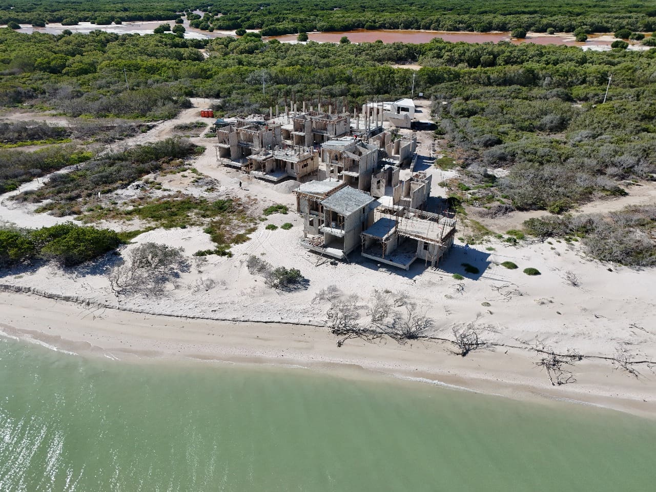 Aerial view of a small, dilapidated building near a sandy beach and green vegetation.