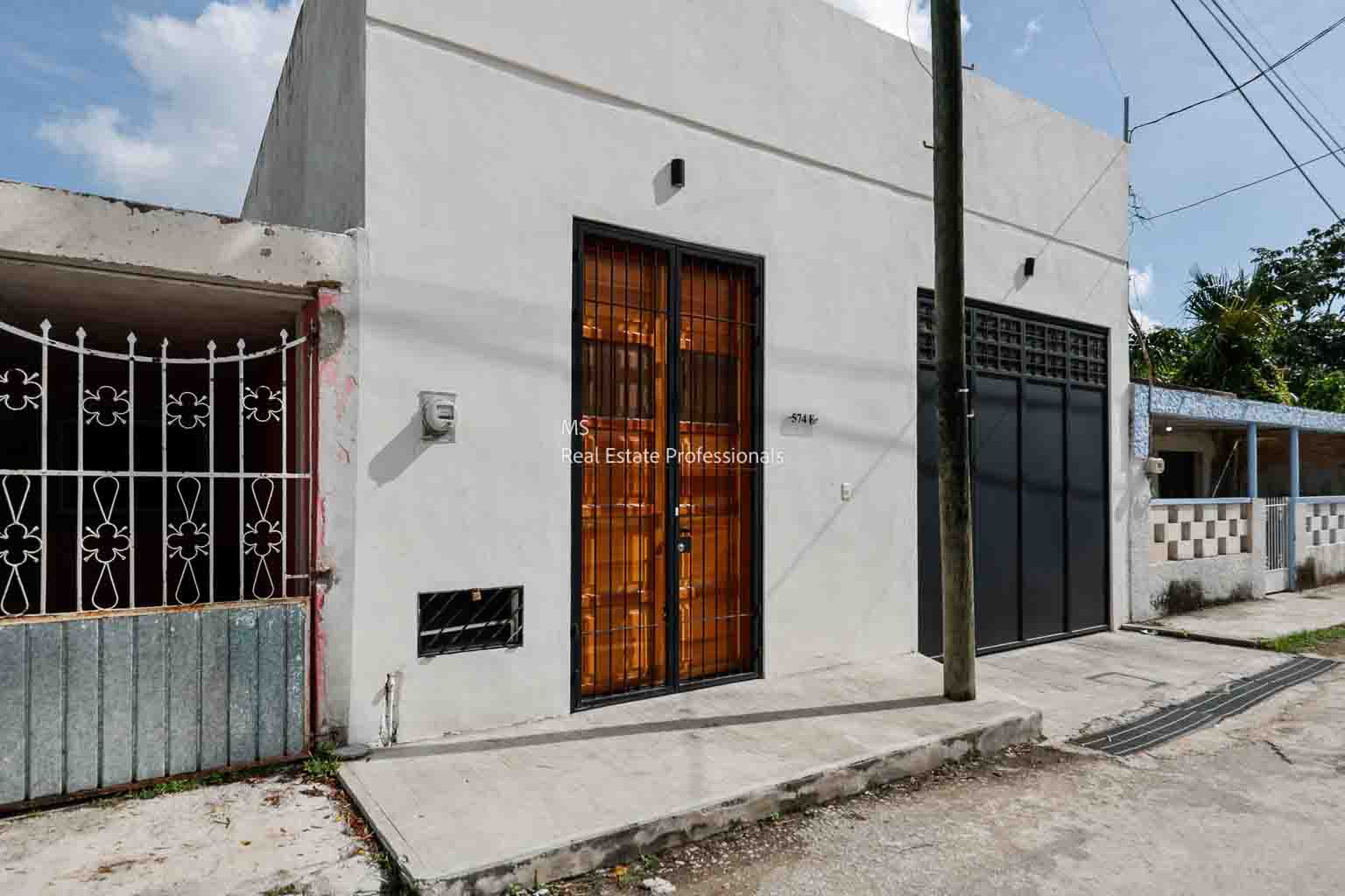 A modern wooden door on a white concrete wall with a sidewalk in front.