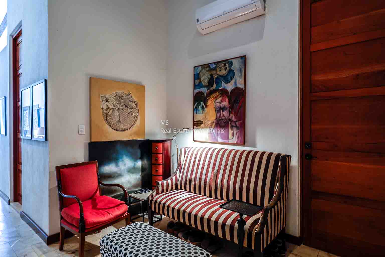 Cozy room with striped sofa, red chair, and wall art under an air conditioner.