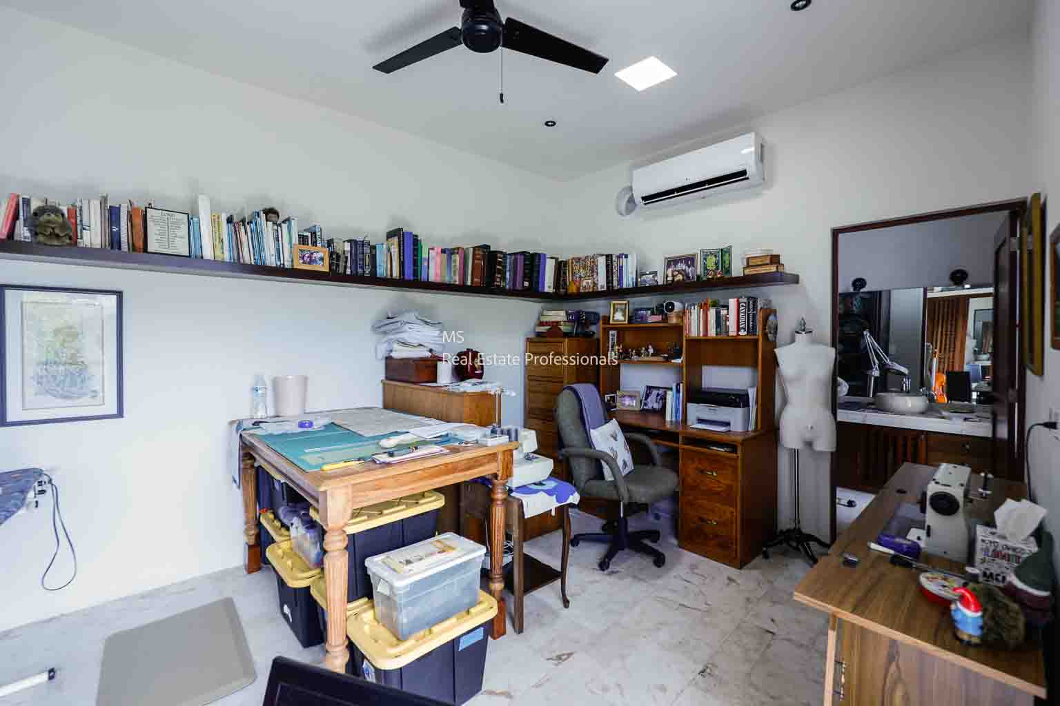 A study room with wooden desks, bookshelves, and office chairs under a ceiling fan.