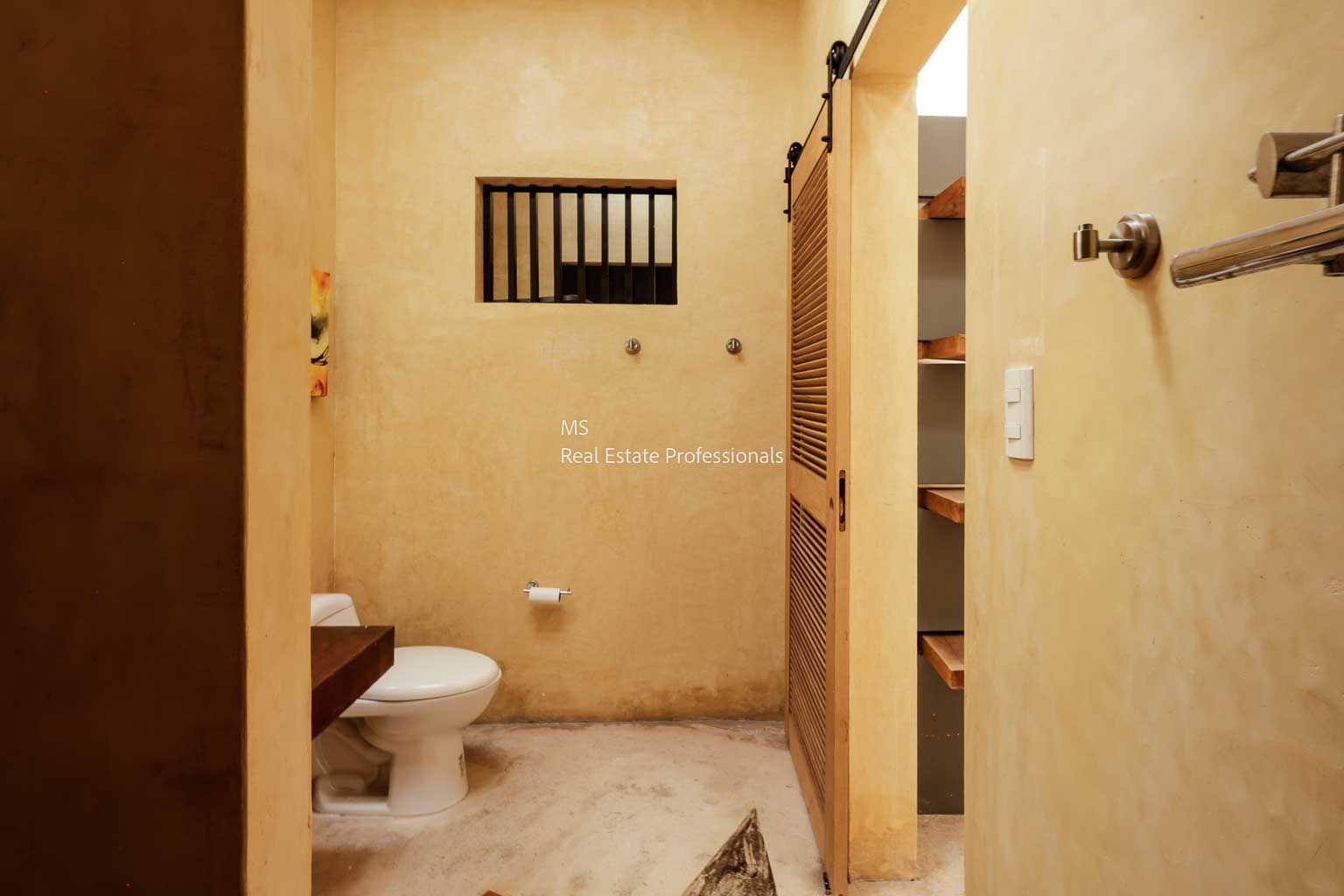 Simple, small beige bathroom with basic fixtures and a barred window.