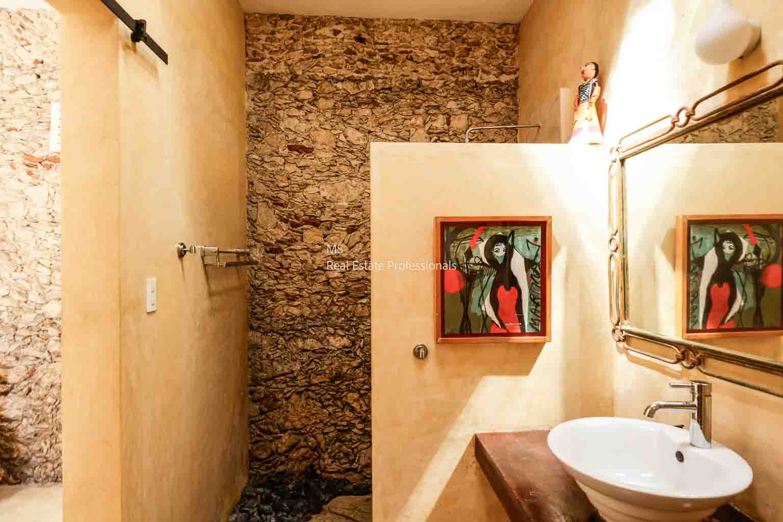 Cozy rustic bathroom with stone wall and framed artwork.