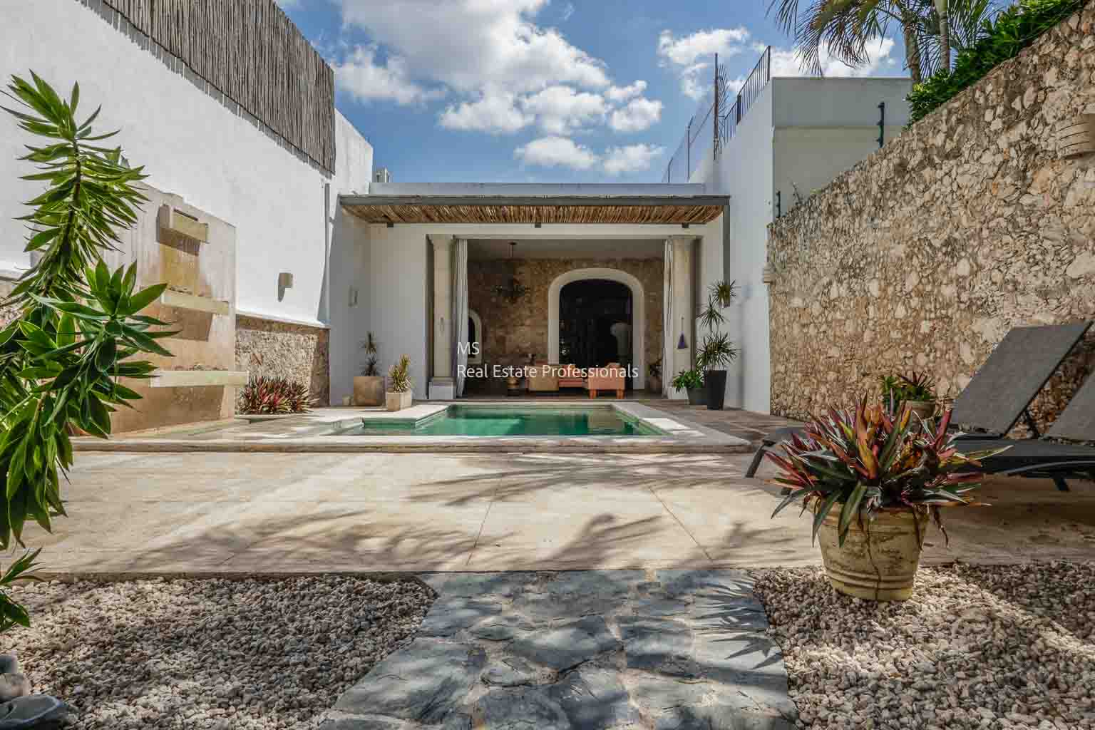 Elegant courtyard with a pool and rustic stone walls under a blue sky.