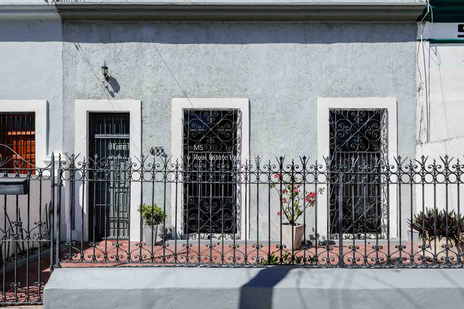Three black doors on a light gray building behind a metal fence.