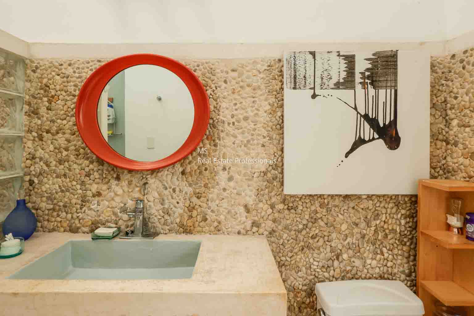 Modern bathroom with a round red mirror and abstract art.