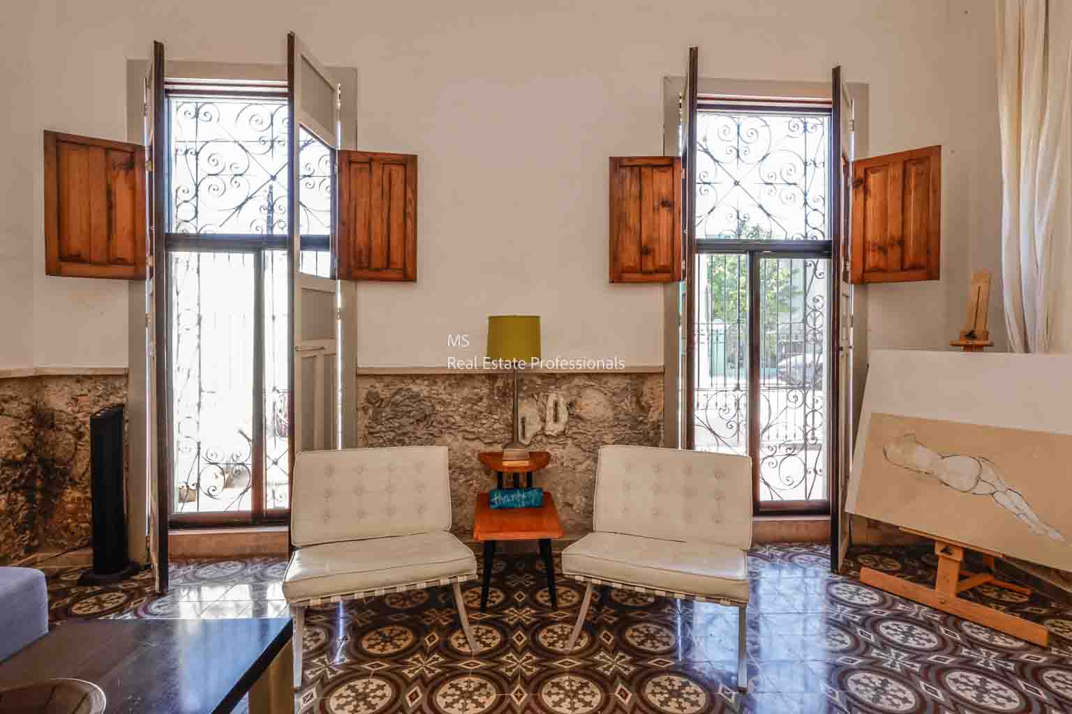 Cozy seating area with two white chairs and wooden window shutters.