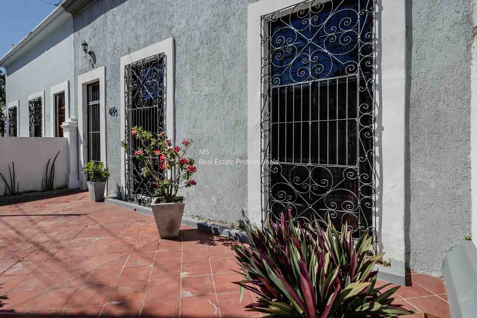 Sunlit courtyard with potted plants and decorative iron window grilles.