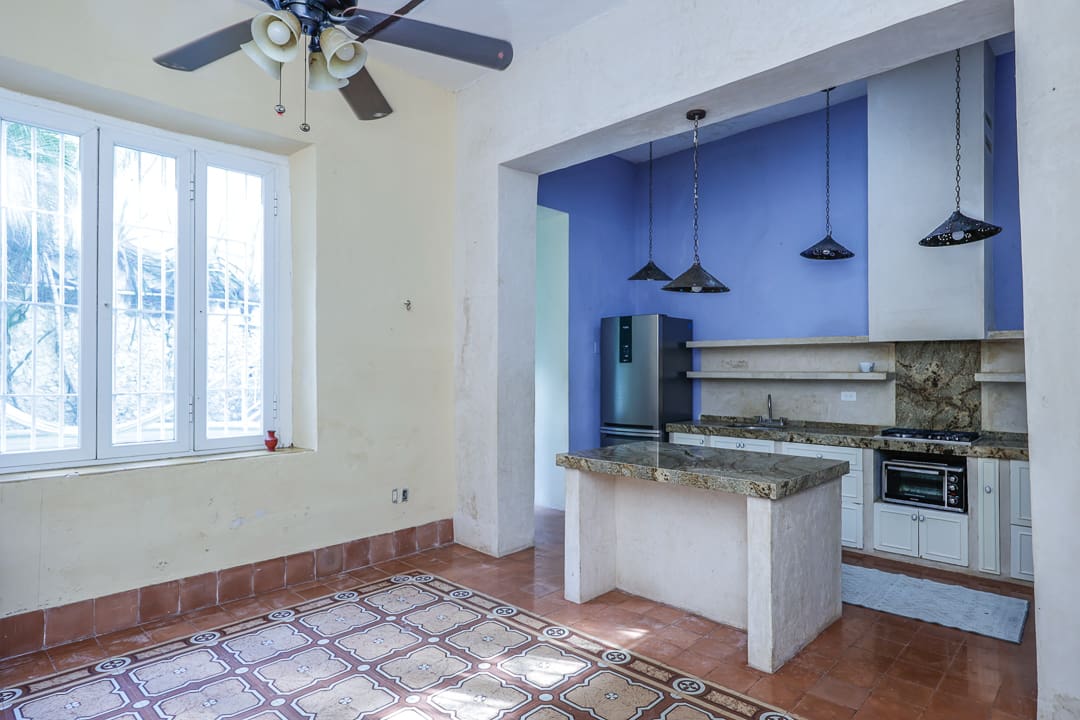 Empty kitchen with white walls and tiled floor, featuring a blue accent wall and ceiling fan.
