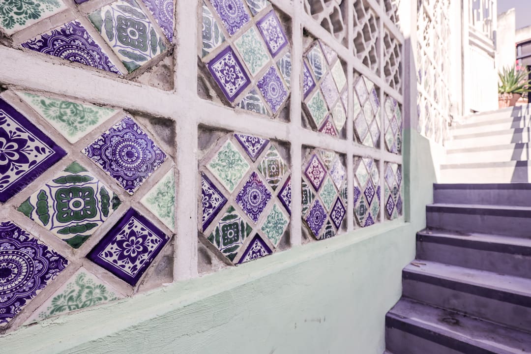 Colorful tiled wall with geometric patterns next to stairs.