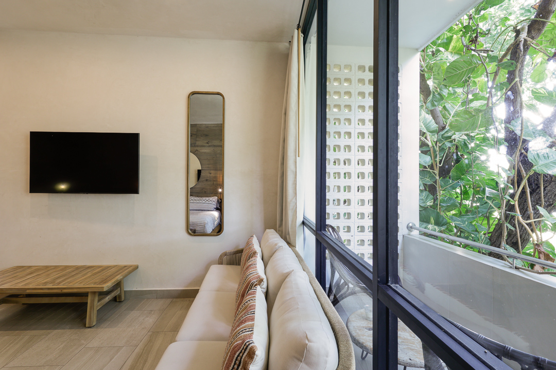 Cozy living room with beige sofa and large windows overlooking greenery.