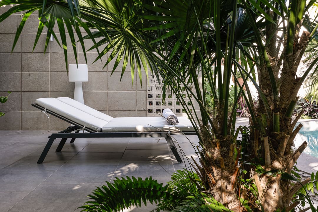 A serene lounge chair beside lush tropical plants and a lamp.