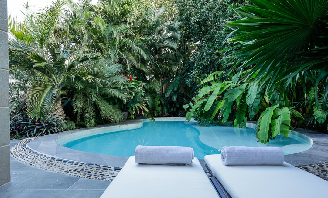 Two lounge chairs with towels by a curved pool surrounded by lush greenery.